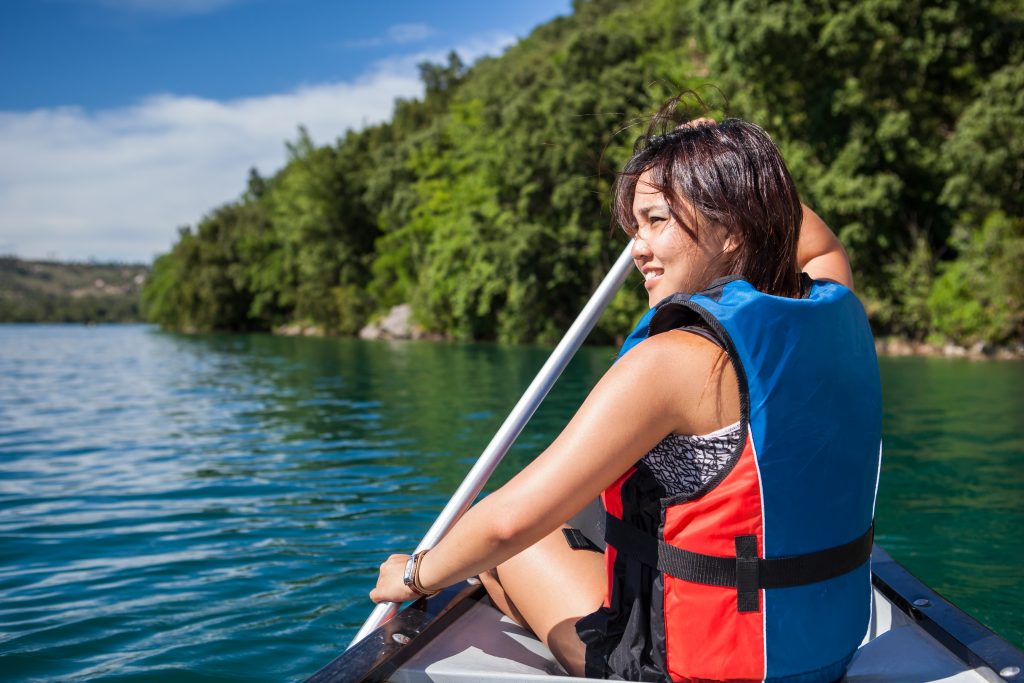 A woman wearing a lifejacket sits at the front of a canoe while holding a paddle